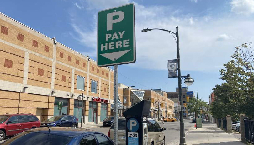 A large parking sign that reads 'pay here' with cars parked around it on a Clarence Street in London, Ontario