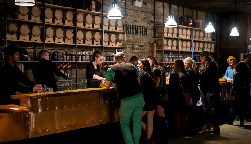 A group of people standing at a bar in Union Ten Distilling's main showroom located in London, Ontario