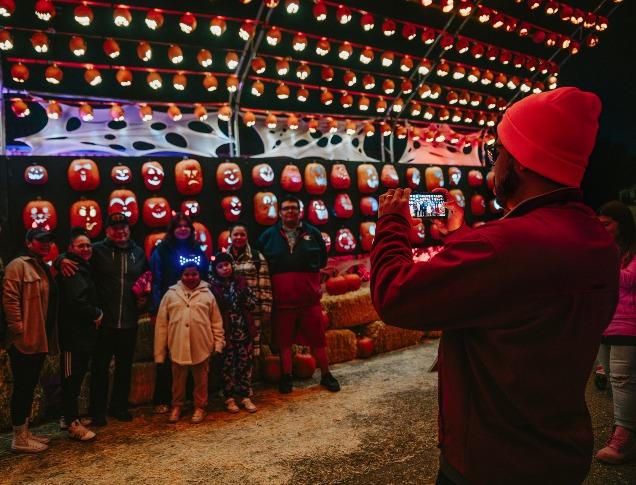 A woman with various children surrounding her near a fall display with hay and pumpkins at Clovermead Adventure Farm