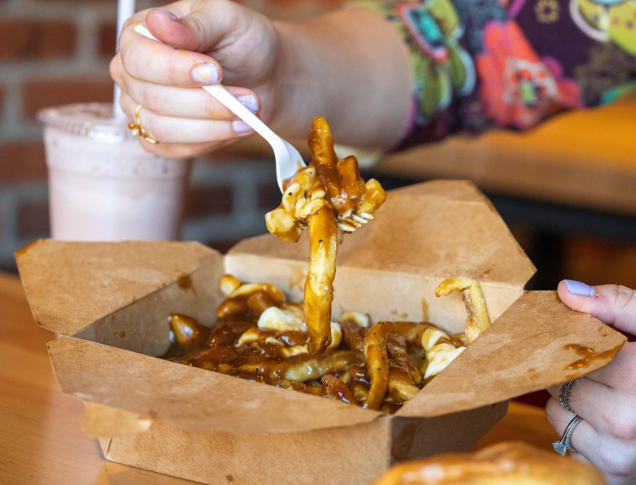 Person eating poutine with a fork inside of a restaurant.