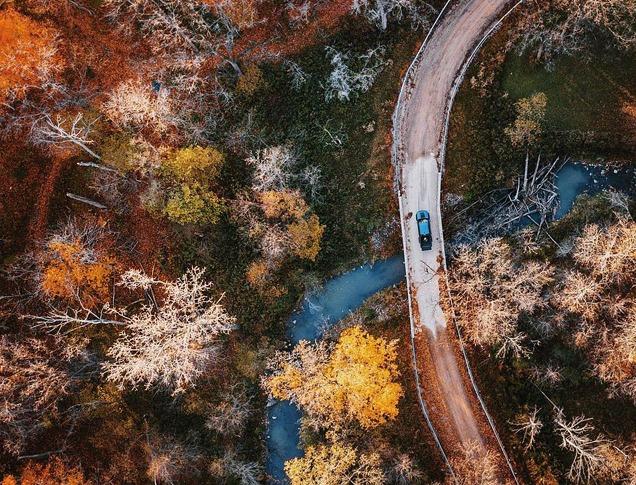 Aerial view of a car driving down a curving road with fall colours in London, Ontario, Canada.