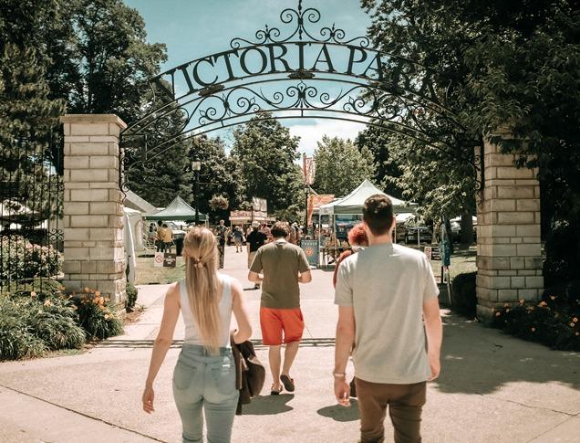 A group of people about to enter the main entrance of Victoria Park on a bright summer day located in London, Ontario
