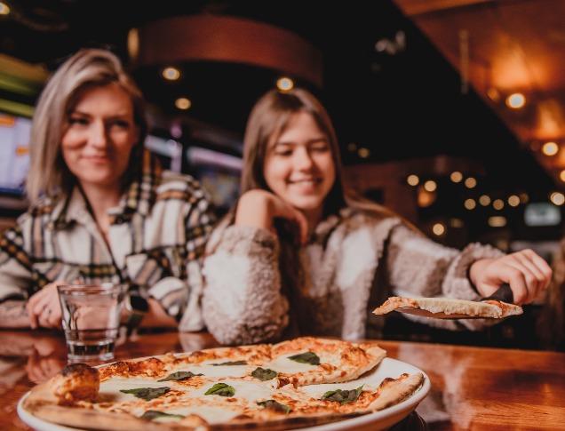 A smiling family shares a margherita pizza at a wooden table in a cozy restaurant.