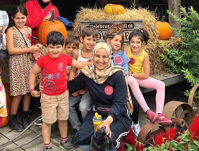 A woman with various children surrounding her near a fall display with hay and pumpkins at Clovermead Adventure Farm