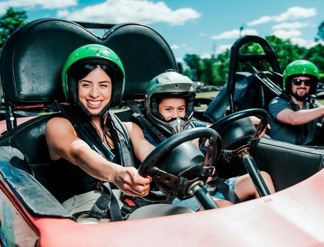 A mother and her young son driving together in a go-cart with the boy's father in a go-cart beside them racing on a track at East Park in London, Ontario, Canada.
