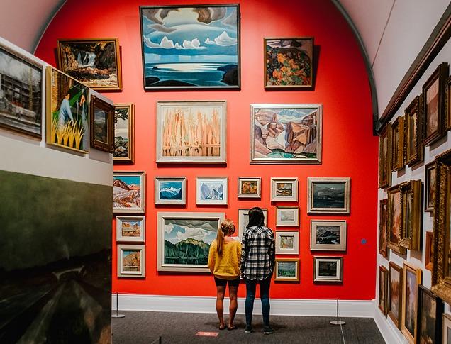 Two women looking at a wall of historic paintings by the group of seven on display in Museum London located in London, Ontario, Canada