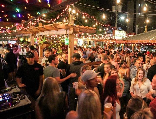 Large groups of people standing and sitting at an outdoor patio in the evening at Barney's and The Ceeps, located in London, Ontario, Canada