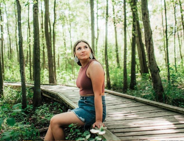 A female sitting at the edge of  the boardwalk path in Sifton Bog looking up to the trees surrounding her located