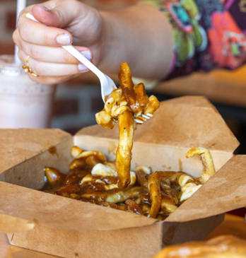 Person eating poutine with a fork inside of a restaurant.