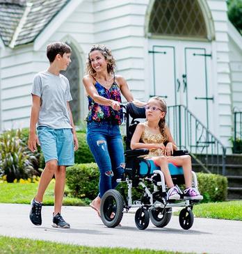 A family with a child in a wheelchair going for a walk on a paved walkway in Storybook Gardens located in London, Ontario