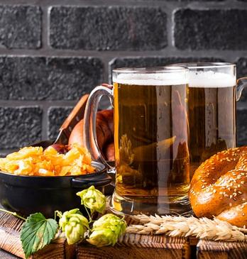 Two glasses of beers and various appetizers displayed on a wooden tray