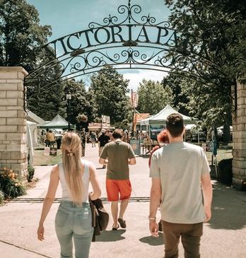 A group of people about to enter the main entrance of Victoria Park on a bright summer day located in London, Ontario