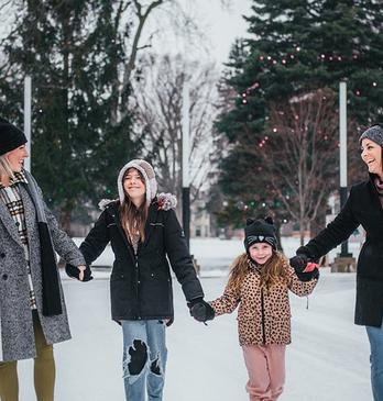 4 people holding hands and skating on the skating rink in Victoria Park locate din London, Ontario