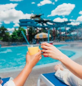 two people sitting by the side of the pool enjoying some sunshine and drinks