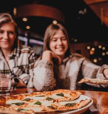A smiling family shares a margherita pizza at a wooden table in a cozy restaurant.