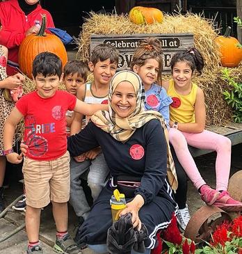 A woman with various children surrounding her near a fall display with hay and pumpkins at Clovermead Adventure Farm