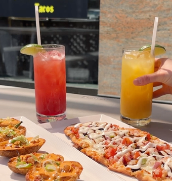 Table with baked potatos, bruschetta and two summery drinks.