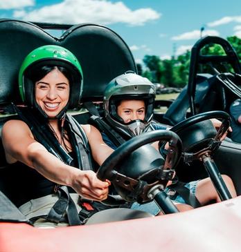 A mother and her young son driving together in a go-cart with the boy's father in a go-cart beside them racing on a track at East Park in London, Ontario, Canada.