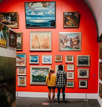 Two women looking at a wall of historic paintings by the group of seven on display in Museum London located in London, Ontario, Canada