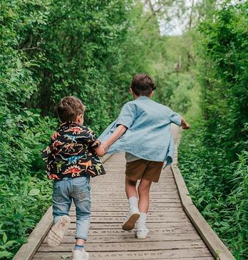 Two young boys holding hands and running down a path in Westminster Ponds located in London, Ontario