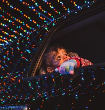 A kid looks out of a car window as the vehicle passes through a magical tunnel of holiday lights.