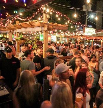 Large groups of people standing and sitting at an outdoor patio in the evening at Barney's and The Ceeps, located in London, Ontario, Canada