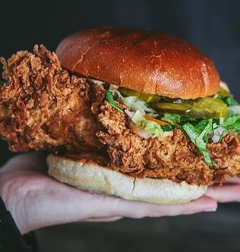 A hand holding a fried chicken burger from BTRMLK located in London, Ontario