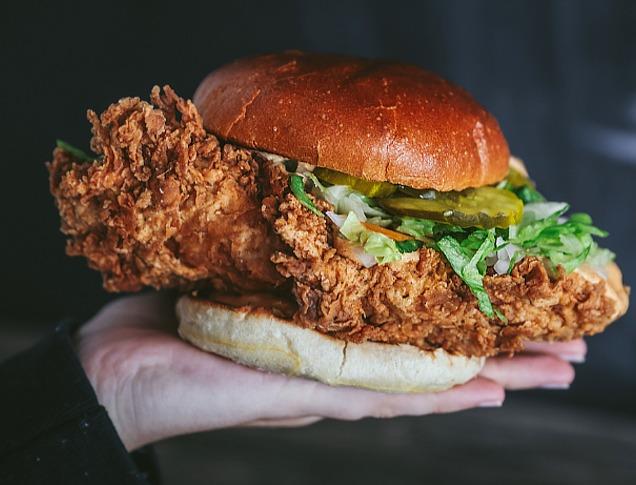 A hand holding a fried chicken burger from BTRMLK located in London, Ontario