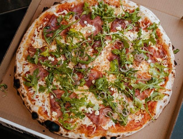 aerial view of a pizza on a black marble table loaded with pepperoni, sausage and basil and a basket of chicken wings