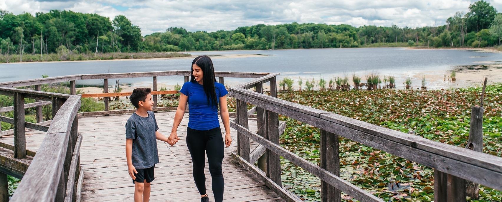 A mother and her son holding hands while walking down a dock in Westminster Ponds located in London, Ontario