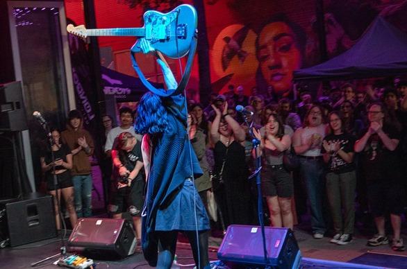 A musician holds up her guitar as a crowd cheers on in excitement during a concert at Market Lane in downtown London, ON