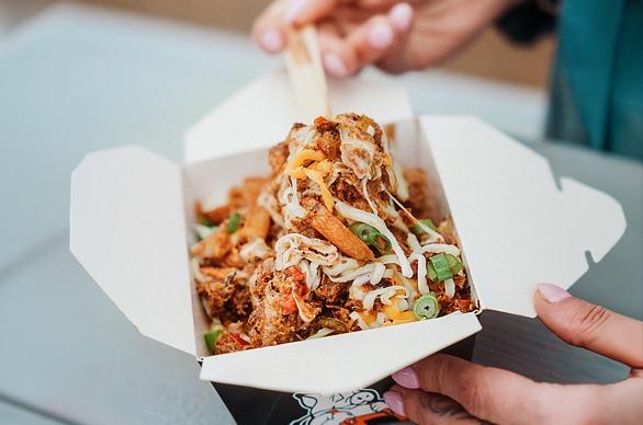 A person eating poutine served in a box
