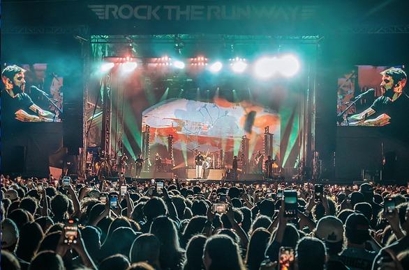 A large crowd gathered outdoors watching musicians play live on a stage at night at Rock the Runway located in London, ON