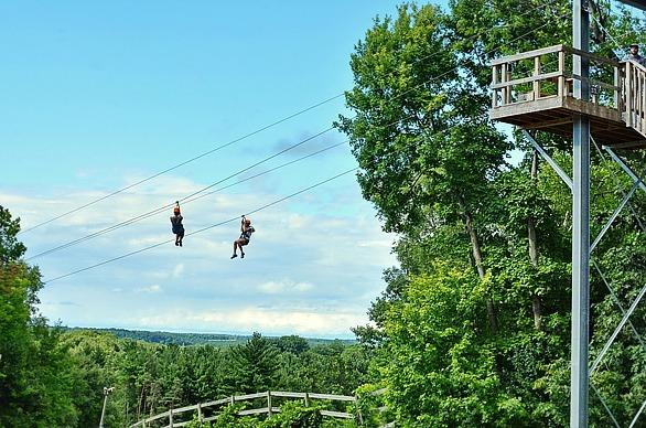 Two people sliding down a zip line with a lush forest in the background at Boler Mountain's Treetop Adventure Park