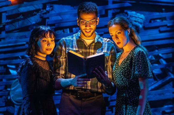 Three actors from the Broadway production Beetlejuice The Musical, looking at a book in awe