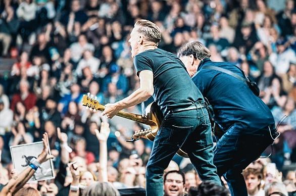 Musician Bryan Adams playing live on stage with a large crowd in the background
