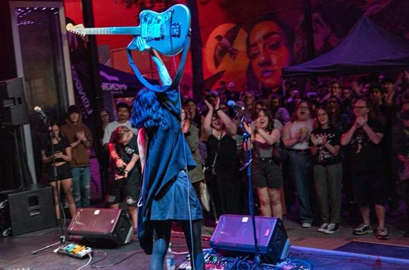 A musician holding up an electric guitar as a crowd cheers on durring a live performance at Dundas Place in London, Ontario