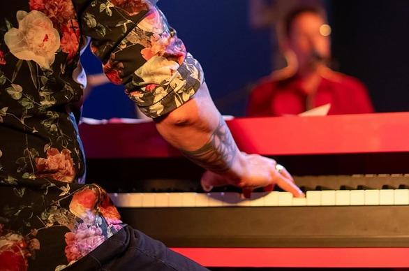 A close up of a piano player from behind and in the background is another paino player blured out