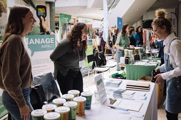 People displaying various products on a table with a large group of people in the background at EarthFest held in London, ON