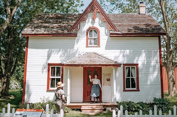 A female standing at the door of an old home waving at Fanshawe Pioneer Village located in London, Ontario