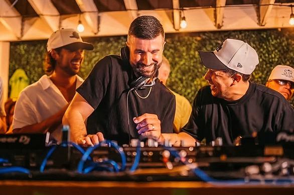 A DJ playing live outdoors with a group of people on stage with him