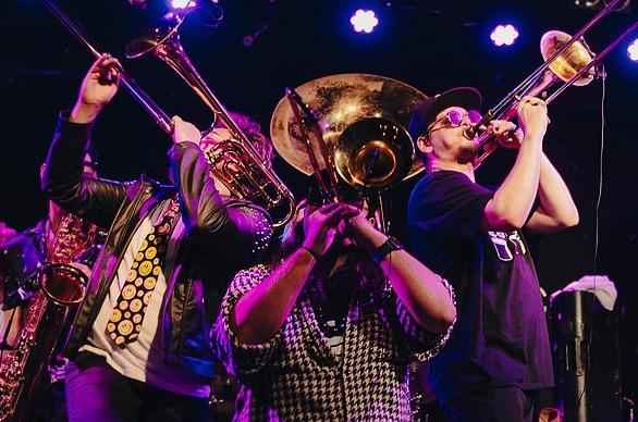 A group of musicians from the band SHOUT! playing trombones and other brass instruments live on stage