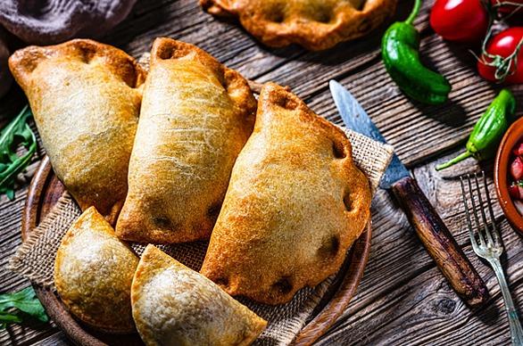 A table top with Empanadas served on a plate surrounded by chilli peppers