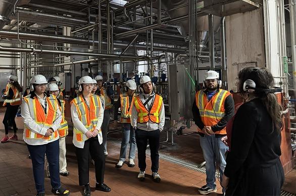 A group of people wearing protective equipment as they listen to a tour guide during the Labatt Brewery tour