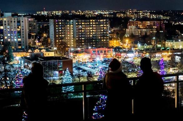 Three people standing on the observation deck of City Hall looking at the lit up trees in Victoria Park located in London, Ontario