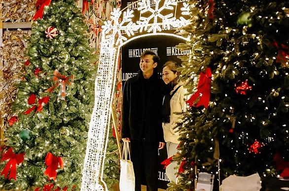 A couple standing between two large Christmas trees decorated with lights and red bows located at 100 Kellogg Lane in London, ON