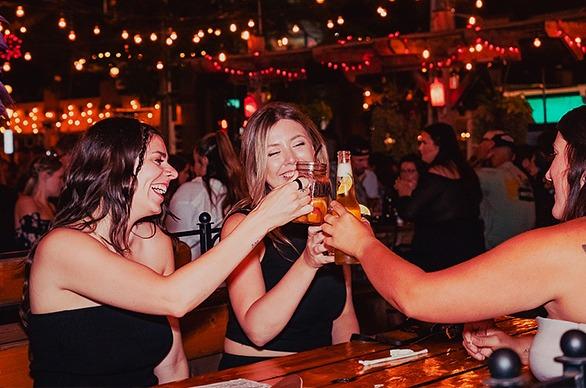 Three females laughing and holding up their glasses at Barney' Patio located in London, Ontario