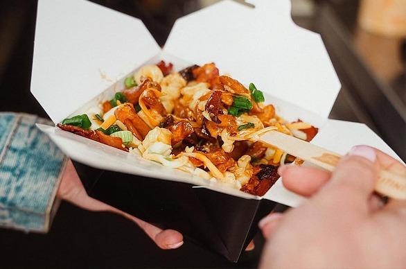 A close up of a person's hands holding a box of poutine