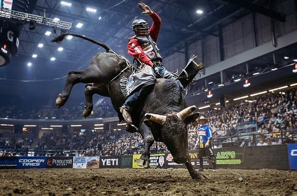 A person riding a bull in a stadium filled with people