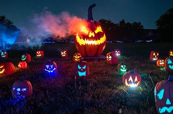 A large glowing, carved pumpkin with several smaller glowing, carved pumpkins surrounding it at night on a field